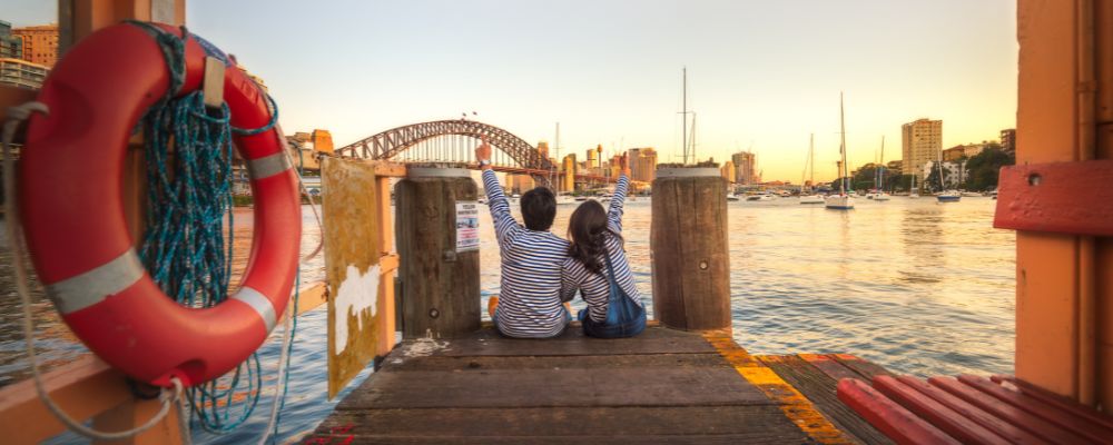 Family sitting on the dock looking towards Sydney Harbour Bridge